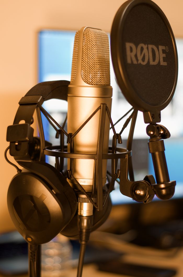 Close-up of a condenser microphone and headphones in a recording studio with soft lighting.